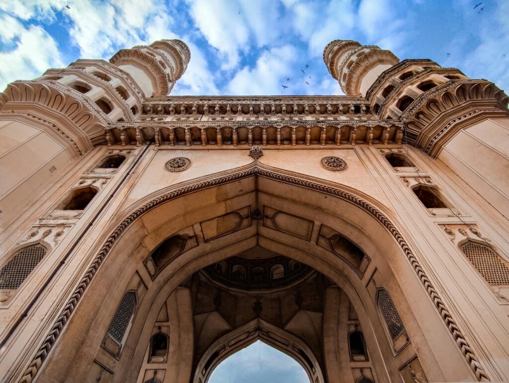 Low angle view of the iconic Charminar monument under a blue sky in Hyderabad, India.