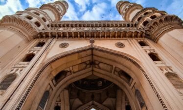 Low angle view of the iconic Charminar monument under a blue sky in Hyderabad, India.